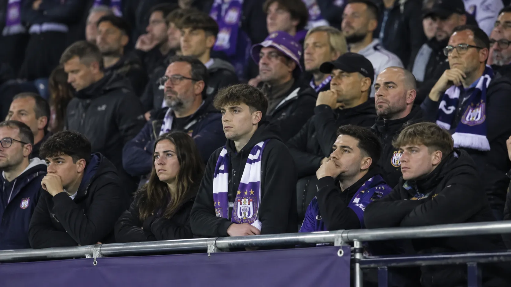 Een groep teleurgestelde Anderlecht-supporters op de tribune met een paars-witte sjaal.