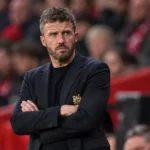 Een Manchester United-trainer staat geconcentreerd langs de zijlijn tijdens een wedstrijd.