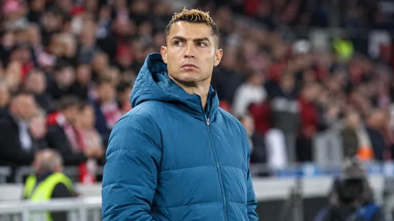 Cristiano Ronaldo in een blauwe jas langs de zijlijn van een voetbalstadion.