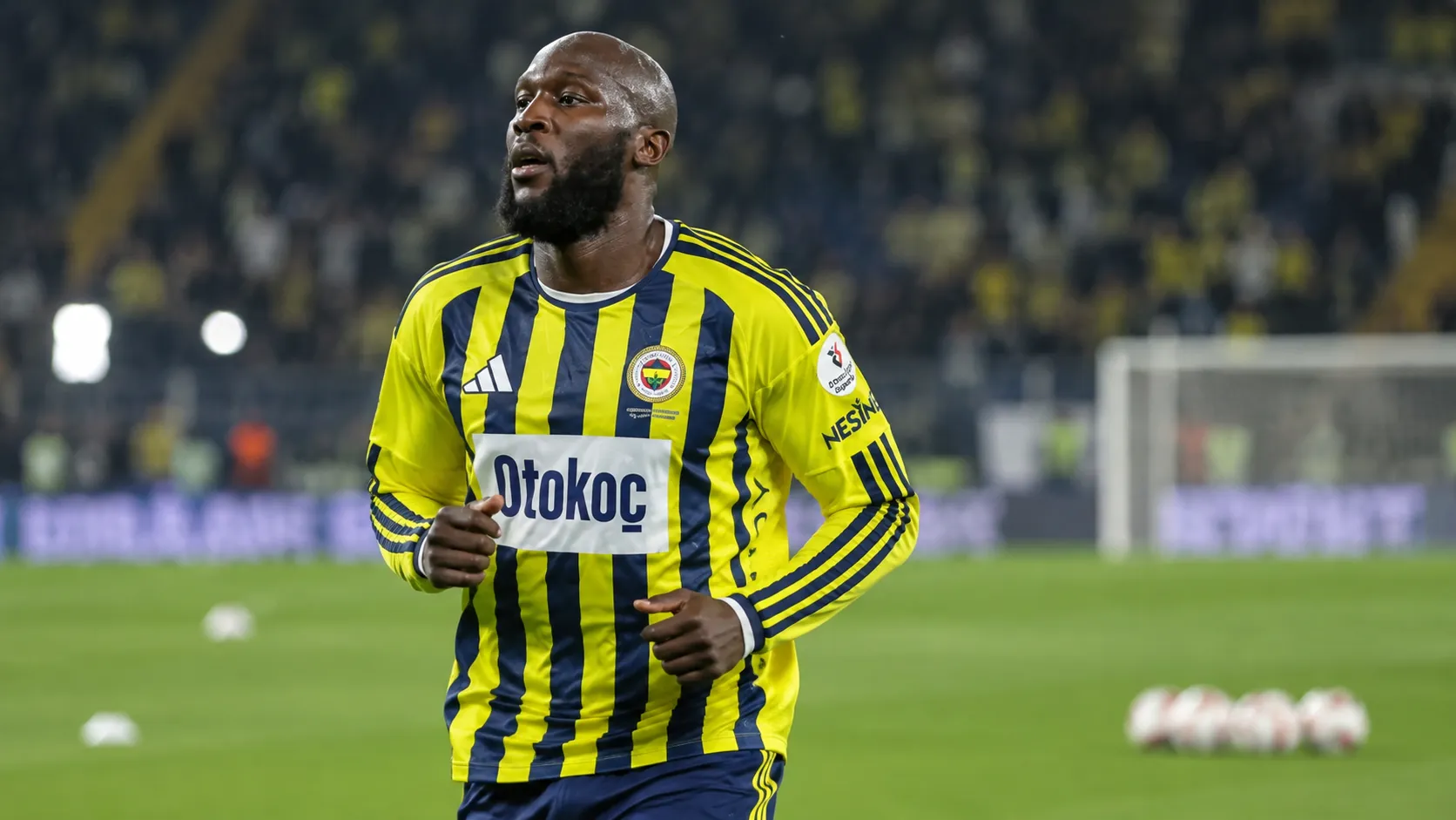 Romelu Lukaku warmt op in een geel-blauw gestreept voetbalshirt op het veld.