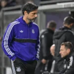 Hein Vanhaezebrouck in paarse sportkleding naast de technische zone van een voetbalstadion.