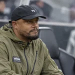 Vincent Kompany zit in een olijfgroene jas op de technische bank van een voetbalstadion.