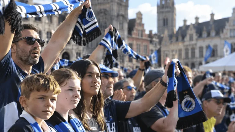 Een groep Club Brugge-supporters heft blauw-zwarte sjaals omhoog in een buitenomgeving.