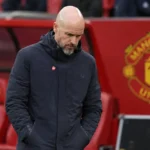 Erik ten Hag in een donkere jas langs de zijlijn van een voetbalstadion.