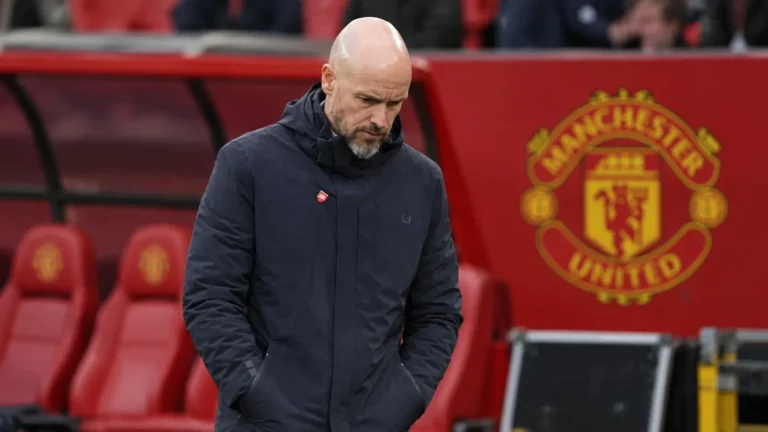 Erik ten Hag in een donkere jas langs de zijlijn van een voetbalstadion.