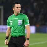 Een scheidsrechter in groen tenue staat vlak voor een wedstrijd op het veld.