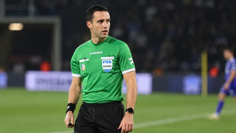 Een scheidsrechter in groen tenue staat vlak voor een wedstrijd op het veld.