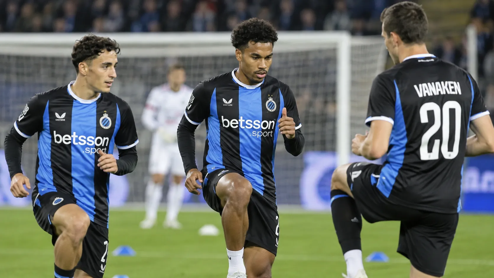 Club Brugge-spelers in blauw-zwarte shirts tijdens een geconcentreerde opwarming op het veld.