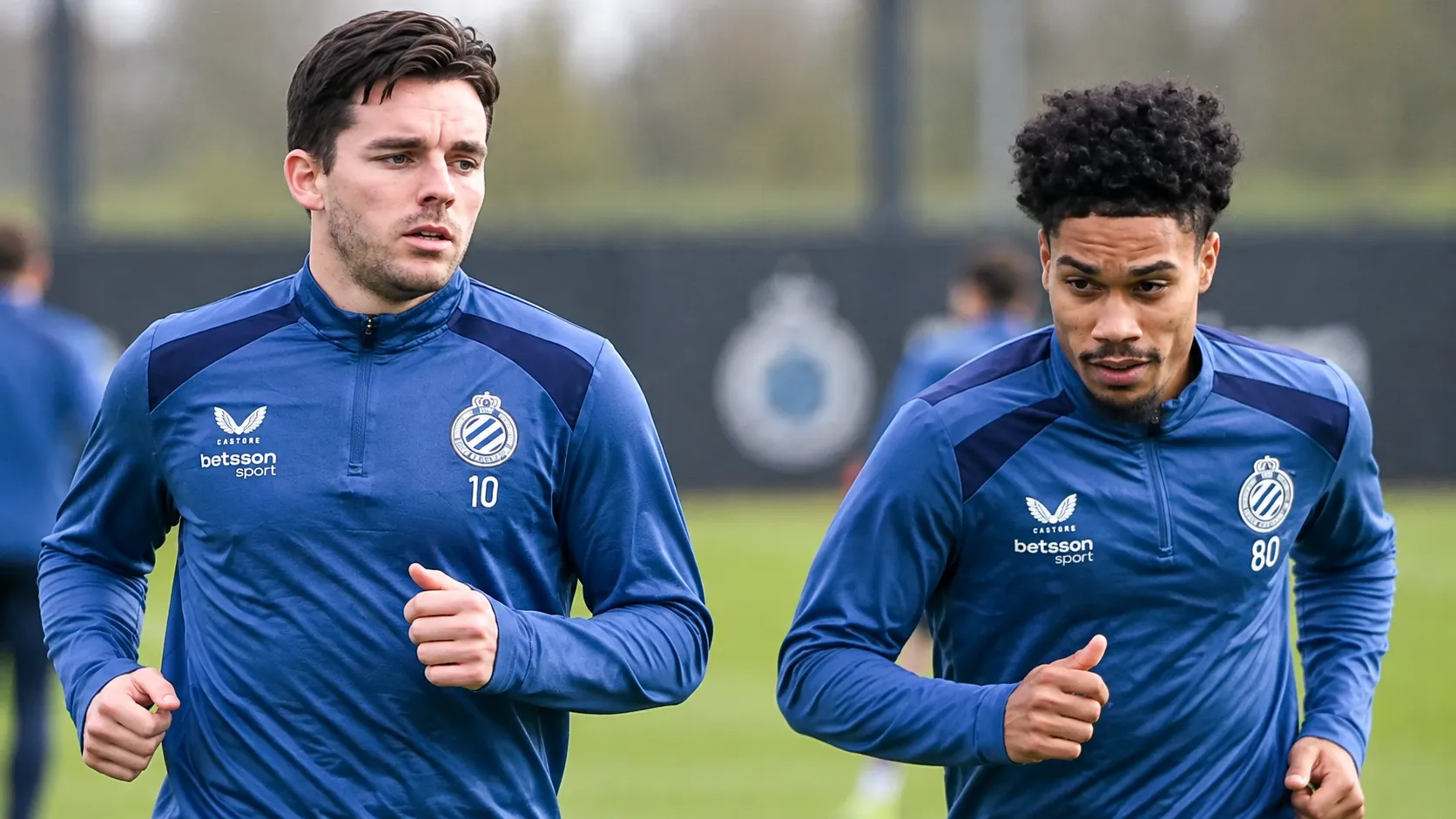 Twee voetballers in blauwe trainingstoppen tijdens een oefensessie op het trainingsveld.