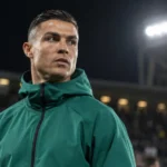 Cristiano Ronaldo in een donkergroene jas aan de zijlijn van een stadion bij avondlicht.