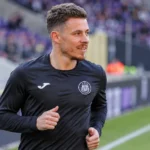 Een voetballer in een donker trainingsshirt tijdens een opwarming in een stadion.