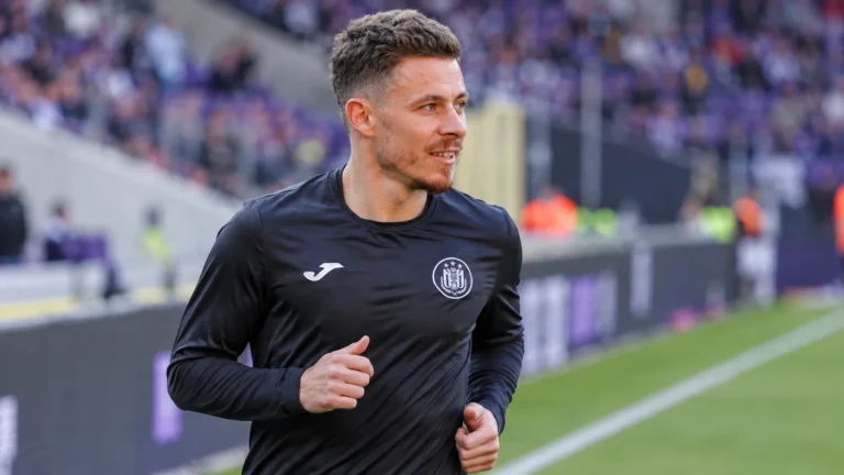Een voetballer in een donker trainingsshirt tijdens een opwarming in een stadion.