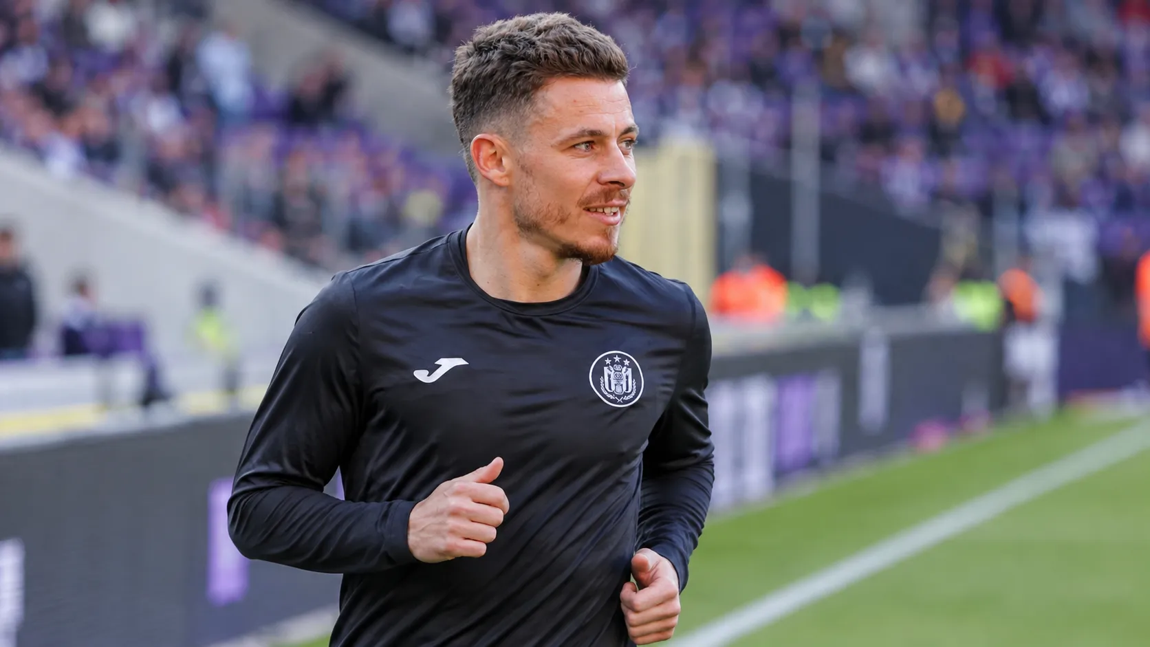 Een voetballer in een donker trainingsshirt tijdens een opwarming in een stadion.