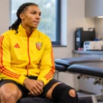 Ismaëlo Ganiou in een gele trainingsjas van RC Lens in een medische herstelruimte.