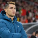 Cristiano Ronaldo in een blauwe jas langs de rand van het veld.