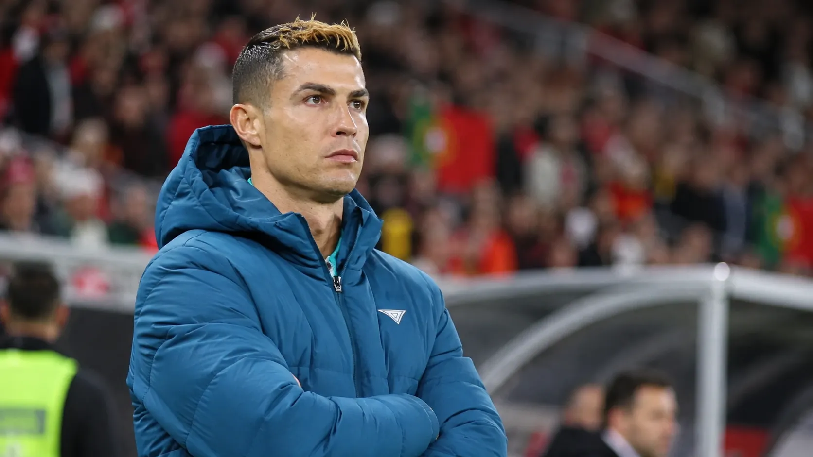 Cristiano Ronaldo in een blauwe jas langs de rand van het veld.