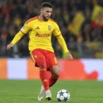 Een speler van RC Lens in geel-rood tenue controleert de bal op het veld.
