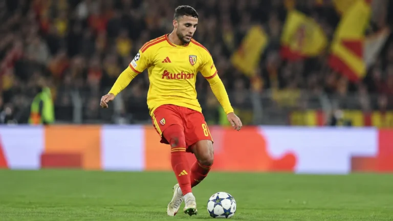 Een speler van RC Lens in geel-rood tenue controleert de bal op het veld.