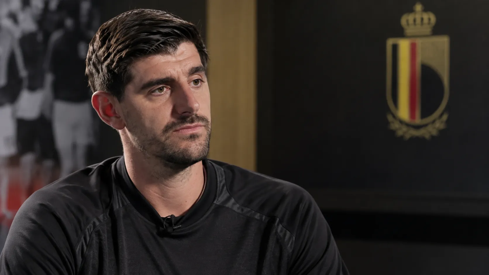 Thibaut Courtois tijdens een rustig media-interview in een ruimte met een subtiel embleem van de Belgische nationale ploeg.