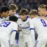 Een groep Anderlecht-spelers verzameld in een hechte kring in witte wedstrijdshirts.