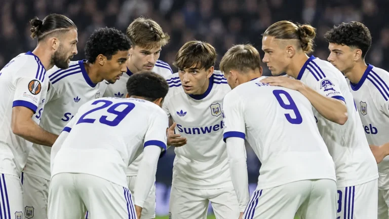 Een groep Anderlecht-spelers verzameld in een hechte kring in witte wedstrijdshirts.