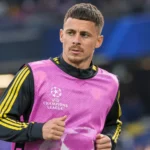 Thorgan Hazard warmt op in een roze hesje in een voetbalstadion.