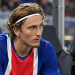 Mika Godts zit in zijn wedstrijdkleding op de bank naast het veld.