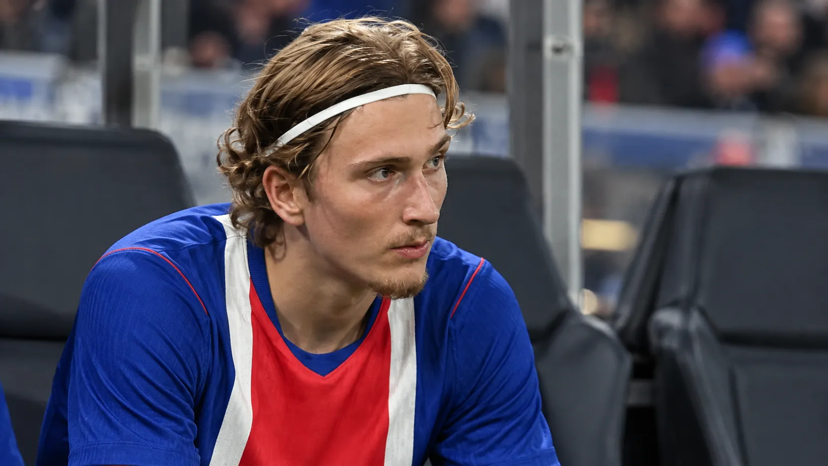 Mika Godts zit in zijn wedstrijdkleding op de bank naast het veld.