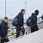 Een groep STVV-reizigers in donkerblauwe sportkleding stapt aan een luchthaven een vliegtuig in.