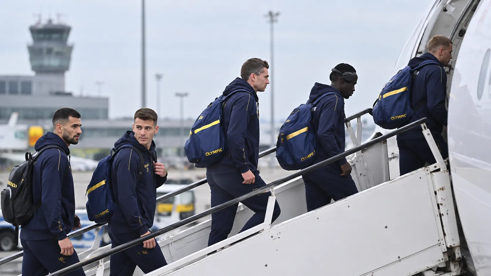 Een groep STVV-reizigers in donkerblauwe sportkleding stapt aan een luchthaven een vliegtuig in.