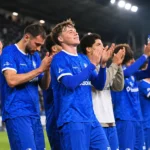 Een groep KAA Gent-spelers in blauwe shirts applaudisseert samen langs het veld.