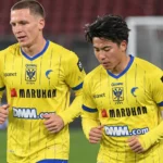 Twee STVV-spelers in gele tenues tijdens de opwarming op het veld.