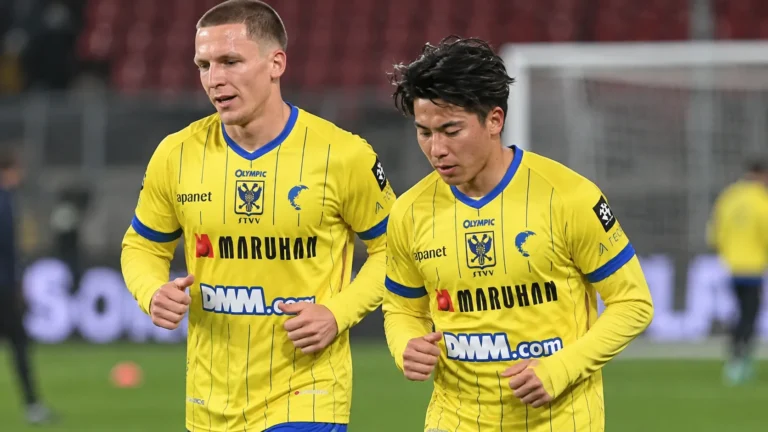 Twee STVV-spelers in gele tenues tijdens de opwarming op het veld.