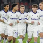 Anderlecht-spelers in witte wedstrijdshirts tijdens de opwarming op het veld.