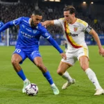 Een speler van RC Lens in duel met een speler van Club Brugge tijdens een avondwedstrijd.