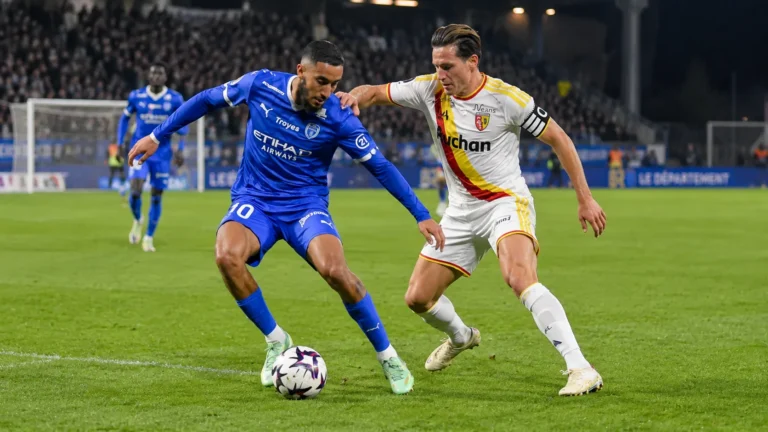 Een speler van RC Lens in duel met een speler van Club Brugge tijdens een avondwedstrijd.