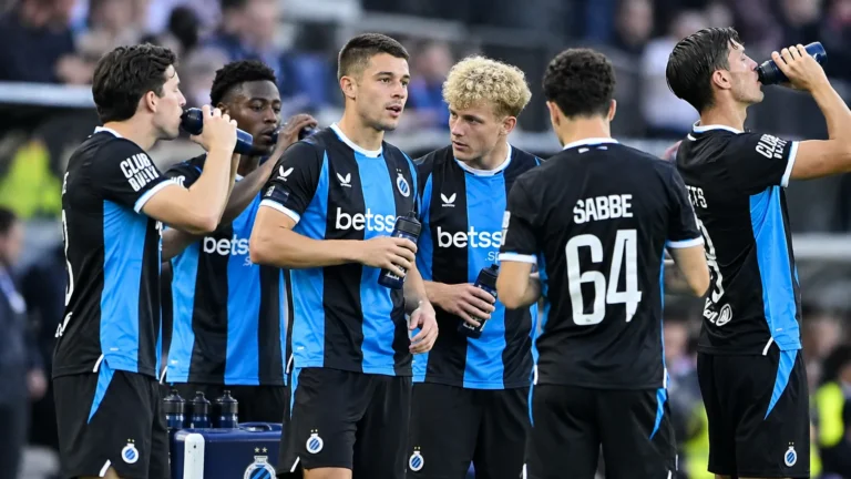 Een groep Club Brugge-spelers drinkt water aan de zijlijn in zwart-blauwe tenues.