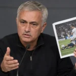 José Mourinho spreekt op een persconferentie terwijl hij afgedrukte wedstrijdfoto’s vasthoudt.