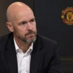Erik ten Hag tijdens een rustig media-interview met een Manchester United-embleem op de achtergrond.