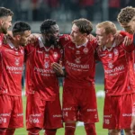 Een groep spelers in rode wedstrijdkleding vormt een hechte kring tijdens de opwarming.