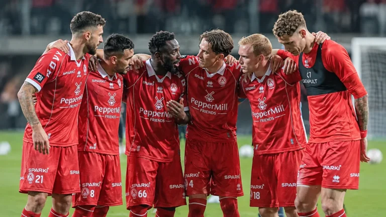 Een groep spelers in rode wedstrijdkleding vormt een hechte kring tijdens de opwarming.