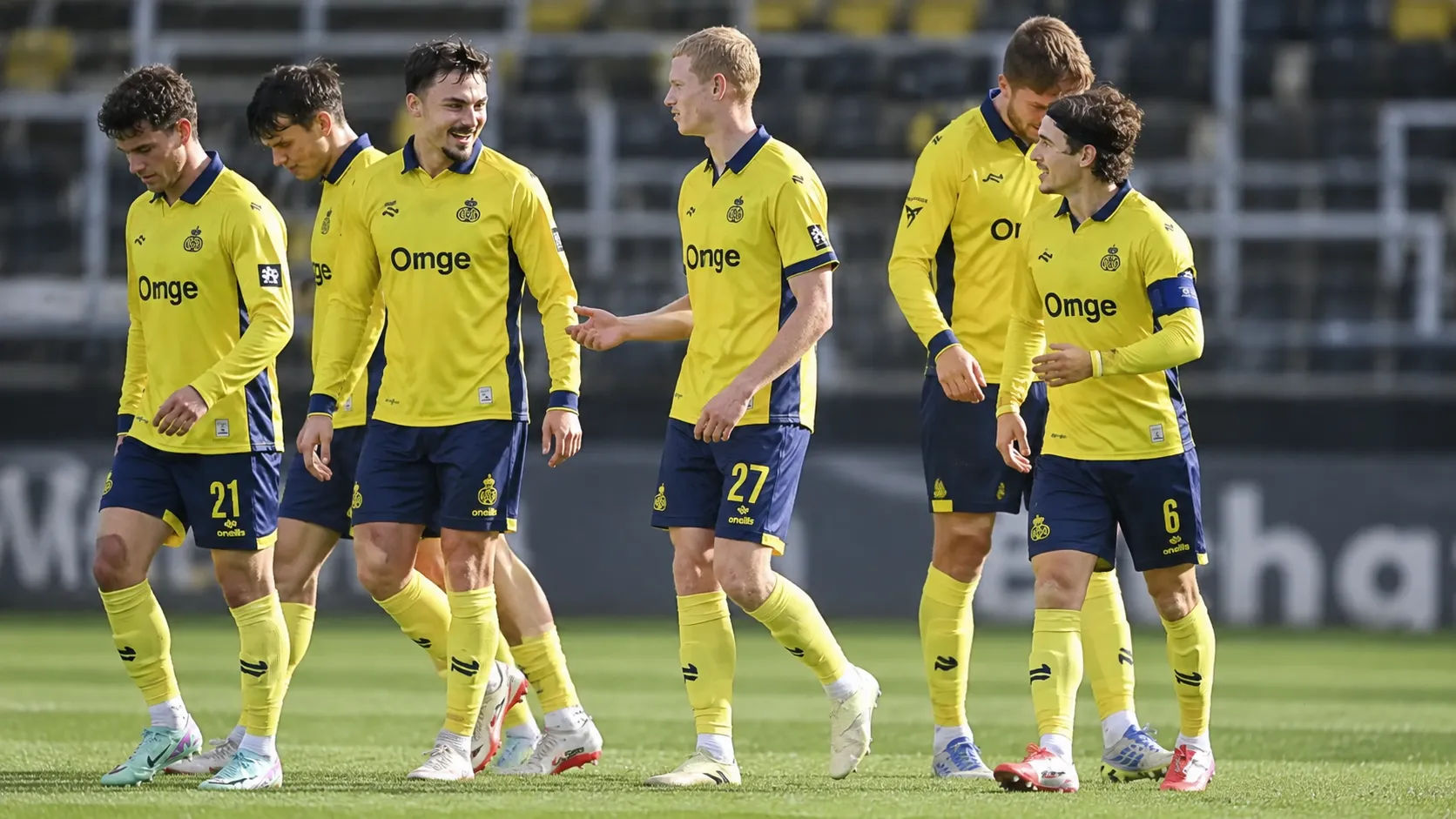 Een groep voetballers in gele shirts en donkerblauwe shorts loopt samen over het veld.