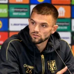 Visar Musliu van STVV spreekt tijdens een persmoment in een donkere clubjas.