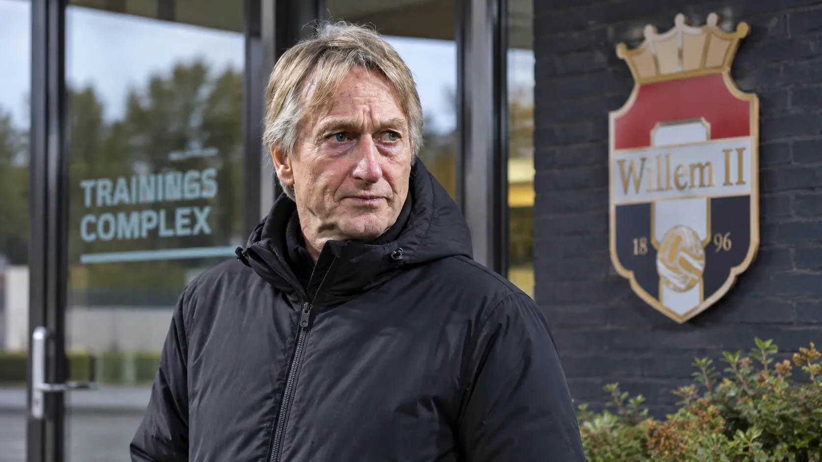 Adrie Koster in een neutrale jas aan de ingang van het trainingscomplex van Willem II.
