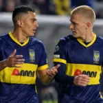 Twee voetballers in donkerblauwe shirts met gele details overleggen samen op het veld.