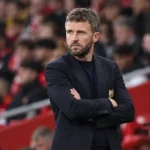 Een Manchester United-coach in donkere kleding langs de zijlijn tijdens een wedstrijd.