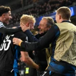 Spelers en stafleden van Club Brugge vieren samen aan de zijlijn van een avondwedstrijd.