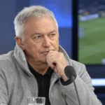 Een grijze voetbalanalist aan een microfoon in een televisiestudio.