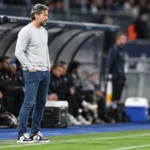 Rik De Mil staat in de technische zone langs het veld bij een wedstrijd van KAA Gent.