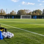Leeg oefenveld met een blauw-zwart Club Brugge-embleem op het trainingshek.